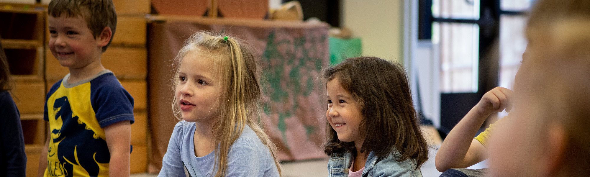 three children sitting on a rug listening in children's school