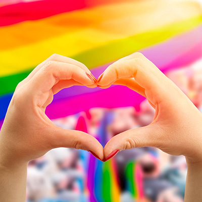 Hands making the heart symbol with rainbow colors in the background