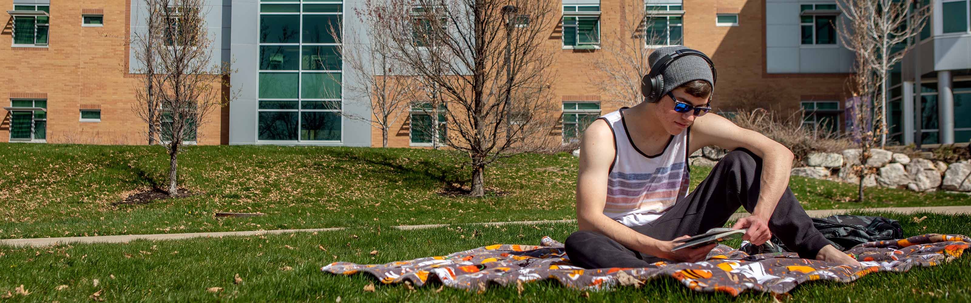 Weber State University student sitting outside on campus reading a book.