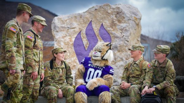 Waldo Wildcat sitting at the W Rock on campus with Cadets in uniform