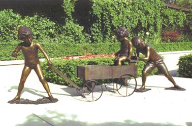 Bronze sculpture depicting children pushing and pulling a wagon with another child inside.